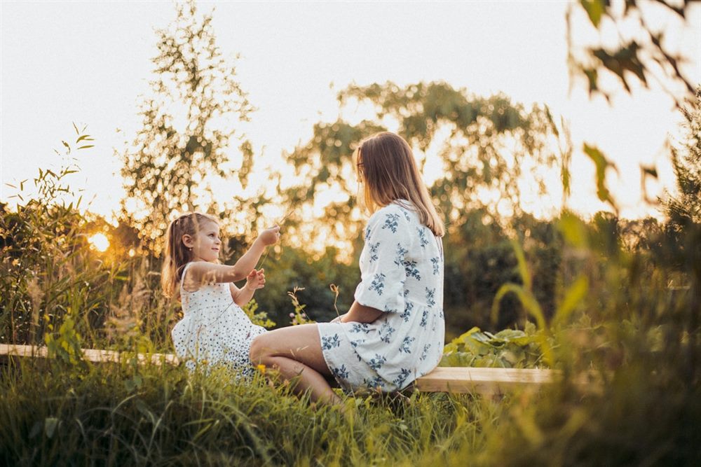 A woman and child sitting together outdoors in warm evening light