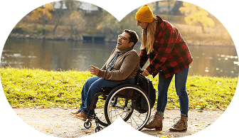 A wheelchair user being supported outdoors beside the water