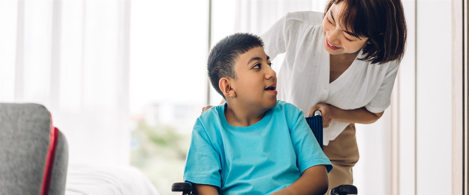 A child using a wheelchair being supported by an adult at home
